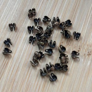 May include: A pile of small, antique gold-toned metal bead caps. The caps have a loop on each side and a small ball on the top.