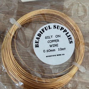 May include: A coil of gold-coloured copper wire for jewellery making. The label reads "BEADIFUL SUPPLIES GILT ON COPPER WIRE 0.60mm 10mt SCIENTIFIC WIRE CO."
