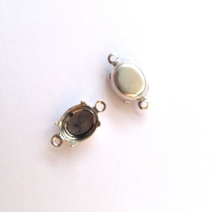 May include: Two silver oval magnetic clasps with small loops at each end. One clasp is open, showing the inside. The clasps are on a white background. These clasps are used for jewellery making.