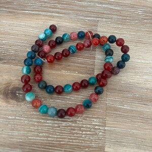 May include: A strand of colourful agate beads in shades of red, blue, and green. The beads are round and have a natural, polished finish.