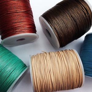 May include: Several spools of cord in a range of colours: red, brown, green, beige, and blue. The cord is neatly wound on white plastic spools. The cords appear to be made of a smooth material, possibly leather. The image is taken from a high angle.