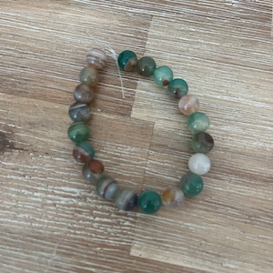May include: A bracelet made of green, brown and white agate beads.