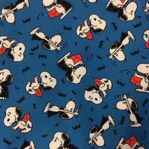 Peut inclure: Un tissu bleu avec un motif r&eacute;p&eacute;t&eacute; d'un chien de dessin anim&eacute; d&eacute;guis&eacute; en vampire. Le chien porte une cape noire et un collier rouge. Il y a aussi de petites chauves-souris noires &eacute;parpill&eacute;es sur le tissu.