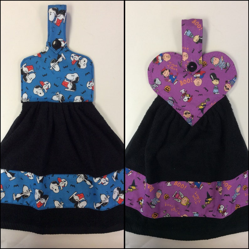 Peut inclure: Deux torchons de cuisine noirs avec une boucle de suspension. L'un a un imprim&eacute; Halloween Peanuts bleu et blanc avec le texte "Trick or Treat". L'autre a un imprim&eacute; Halloween Peanuts violet et blanc avec le texte "Boo!" et "Trick or Treat".