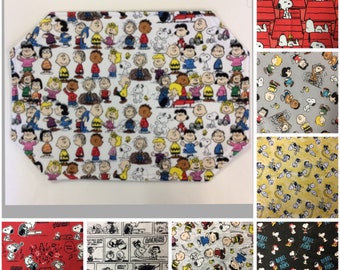 Peut inclure: Un assortiment d'échantillons de tissu mettant en scène divers personnages de Peanuts, notamment Snoopy, Charlie Brown, Lucy et Linus. Les échantillons présentent différents motifs et designs, dont un motif rouge et blanc avec Snoopy dans une niche, un motif de bande dessinée noir et blanc et un motif gris avec des personnages de Peanuts dans diverses poses.