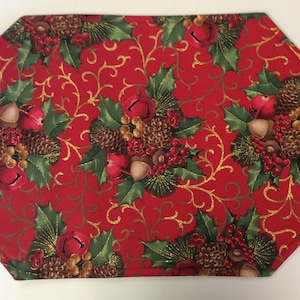 May include: A rectangular Christmas placemat with a red background and a repeating pattern of holly leaves, pinecones, berries, and bells. Gold swirls accent the design, creating a festive holiday theme.