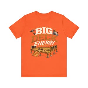 May include: An orange short-sleeve t-shirt featuring a graphic of a wooden deck with a hammer and circular saw. The text BIG DECK ENERGY is printed in large white and brown letters above the illustration of the deck structure and stairs.