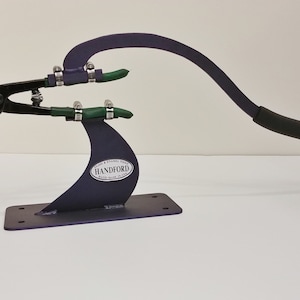 May include: A purple metal tool with a black handle and green rubber tubing. The tool is labeled "HANDFORD" and is used for glass and enamel work.