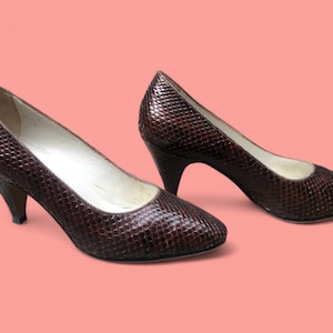 Könnte beinhalten: Ein Paar braune Pumps aus Schlangenleder mit spitzer Zehenpartie.