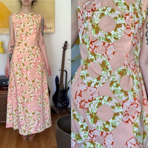Könnte beinhalten: Ein langes, ärmelloses Kleid mit rosa Hintergrund und einem Muster aus grünen, weißen und orangen Kreisen. Das Kleid hat einen taillierten Oberteil und einen fließenden Rock.