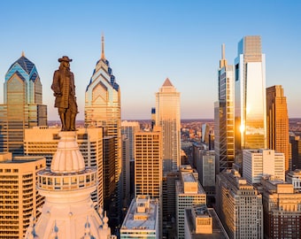 May include: An aerial view of the Philadelphia skyline at sunset, with the statue of William Penn atop City Hall.