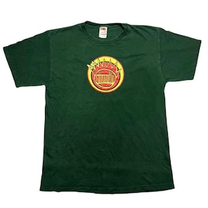 Puede incluir: Camiseta verde oscuro con un diseño gráfico circular. El diseño gráfico presenta un diseño rojo y amarillo con una corona y una forma similar a una parrilla en el centro. La camiseta está hecha de un material suave y tiene mangas cortas.