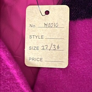 May include: Close-up of a tag attached to a magenta fabric. The tag reads "No. H0010", "SIZE 22/36". The fabric has a plaid pattern with black stripes. The tag is attached with a black string.