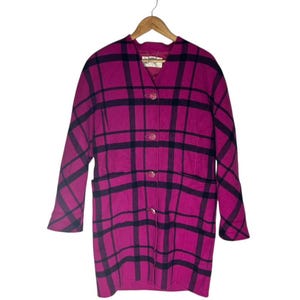 May include: A magenta and black plaid coat with a classic design. The coat features a collared neckline, three buttons, and two front pockets. The coat is hanging on a wooden hanger.