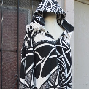 May include: Black and white hooded tunic with a geometric pattern. The tunic has a long, flowing silhouette and a hood with a drawstring.