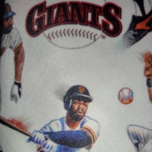 May include: A white tie with a baseball theme. The tie features a baseball with the word "Giants" on it, a baseball player swinging a bat, and a baseball player catching a ball.