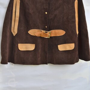 May include: A brown suede cape with a tan suede collar, trim, and pockets. The cape has a button closure and a belt with a buckle.