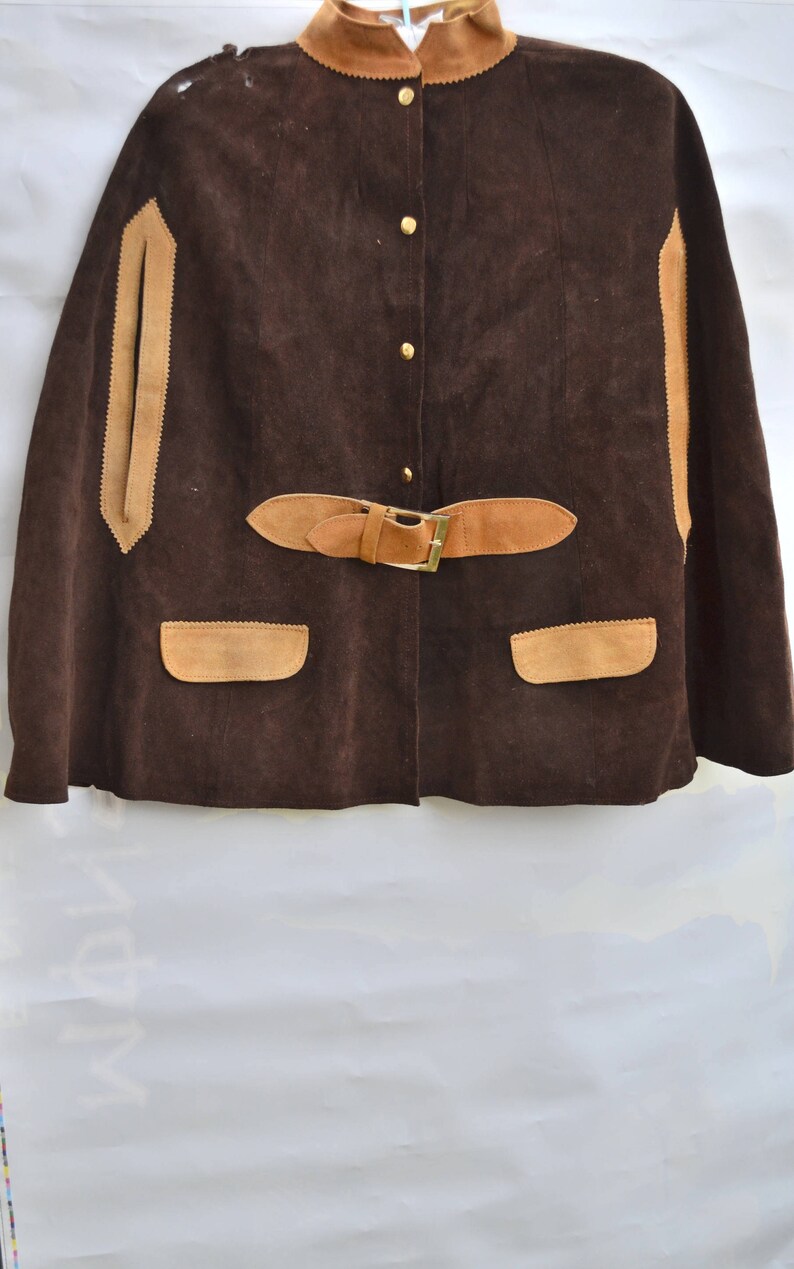 May include: A brown suede cape with a tan suede collar, trim, and pockets. The cape has a button closure and a belt with a buckle.