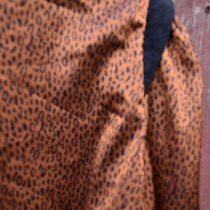 May include: Close-up of a brown fabric with a black leopard print pattern. The fabric is textured and has a soft, drapey feel.