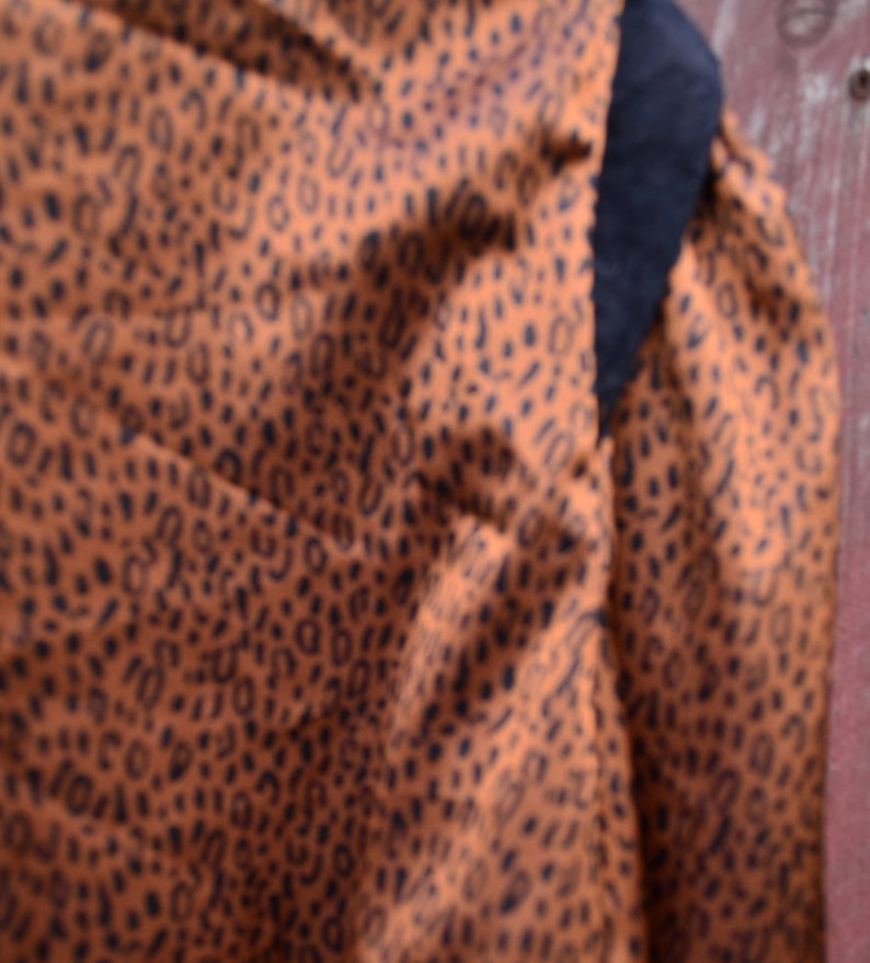 May include: Close-up of a brown fabric with a black leopard print pattern. The fabric is textured and has a soft, drapey feel.