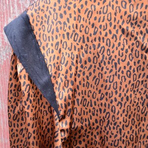 May include: Close-up of a brown fabric with a black leopard print pattern. The fabric has a black trim along the edge.