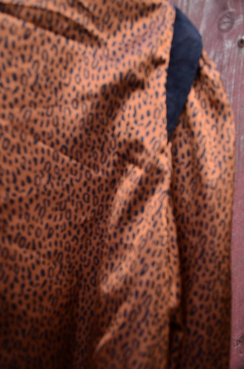 May include: A brown and black patterned fabric with a black trim. The fabric has a subtle sheen and a soft texture.