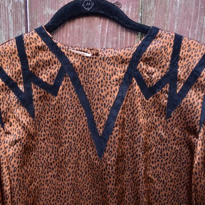 May include: A brown and black leopard print blouse with black trim around the neckline and shoulders. The blouse has a V-neckline and long sleeves.