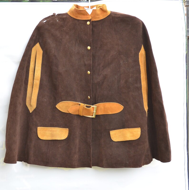 May include: A brown suede cape with a tan suede collar, trim, and belt. The cape has a button closure and two pockets.