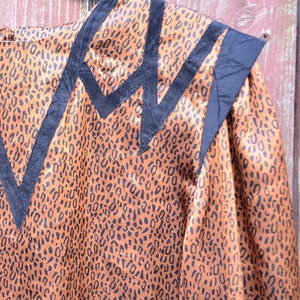 May include: A brown and black leopard print blouse with black trim around the neckline and shoulders. The blouse has a satin-like finish.