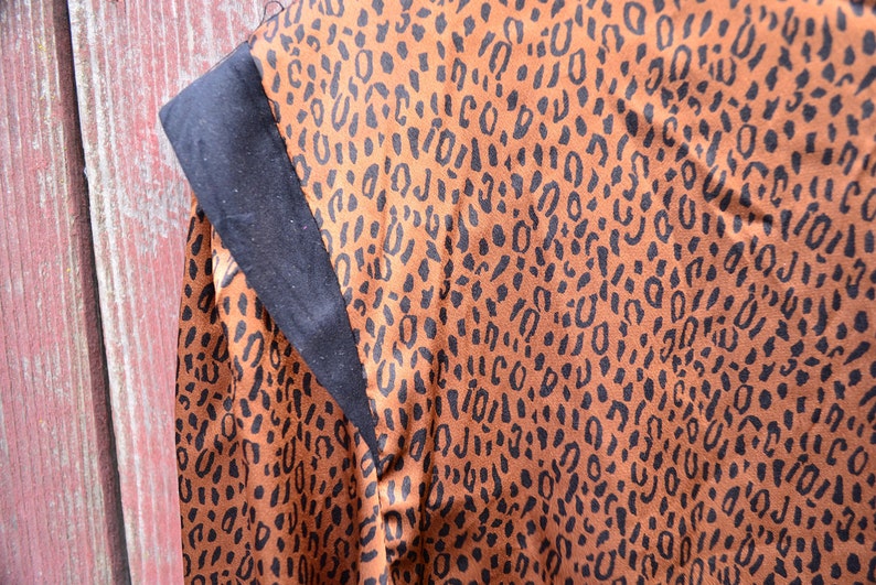 May include: A brown fabric with a black leopard print pattern. The fabric has a black trim along the edge.