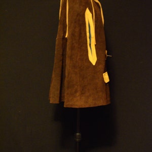 May include: A brown suede jacket with yellow trim and a blue lining. The jacket is on a black stand.