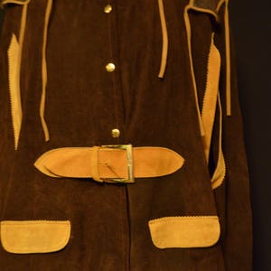 May include: A brown suede jacket with a tan suede trim and a belt. The jacket has a button-up front and two pockets.