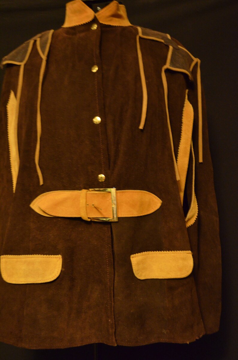 May include: A brown suede jacket with a tan suede trim and a belt. The jacket has a button-up front and two pockets.