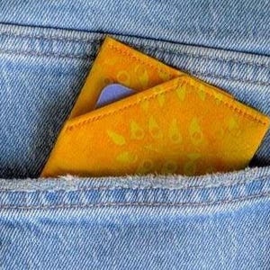 Peut inclure: Gros plan d'une poche de jean bleu clair avec un portefeuille jaune à l'intérieur. Le portefeuille présente un motif cachemire et est partiellement visible. Une carte bleue est également visible. Le jean a des coutures visibles.