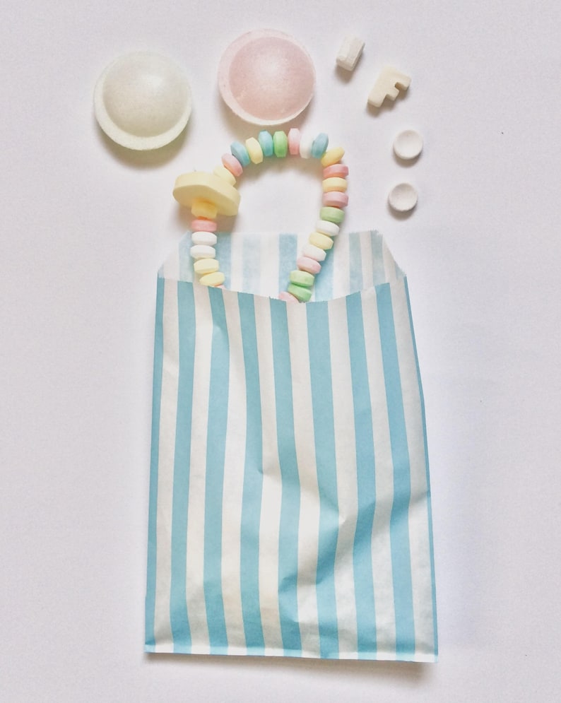 Pu&ograve; includere: Un sacchetto di carta a strisce blu e bianche pieno di caramelle colorate. Le caramelle includono una collana di caramelle color pastello, alcune caramelle rotonde e alcune piccole caramelle bianche.