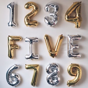Peut inclure: Un ensemble de neuf ballons en feuille d'or et d'argent épellant le mot "1234 FIVE 6789".