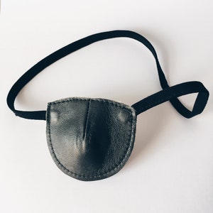 May include: A black leather eye patch with an adjustable strap. The patch is designed to cover one eye.