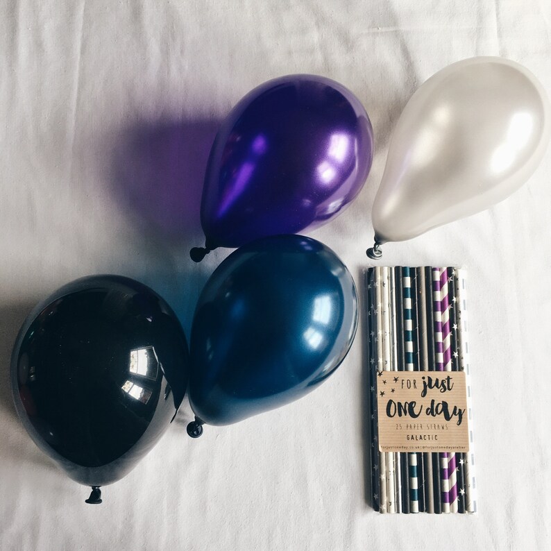May include: Four balloons in black, purple, blue, and white, with a pack of 25 paper straws with a brown label that says "For just one day 25 paper straws Galactic".