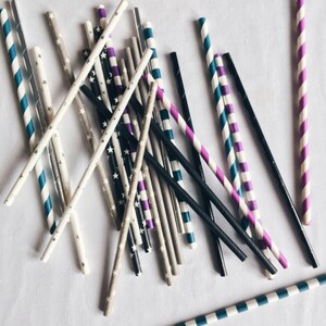 May include: A collection of colorful striped paper straws in various colors, including blue, purple, black, and white. The straws are arranged in a random pattern on a white surface.