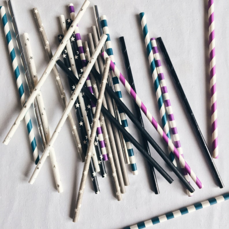 May include: A collection of colorful striped paper straws in various colors, including blue, purple, black, and white. The straws are arranged in a random pattern on a white surface.