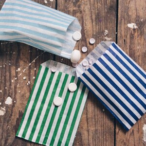 Pu&ograve; includere: Tre sacchetti di carta a righe con caramelle rotonde bianche sparse intorno. I sacchetti sono blu e bianco, verde e bianco e blu e bianco.