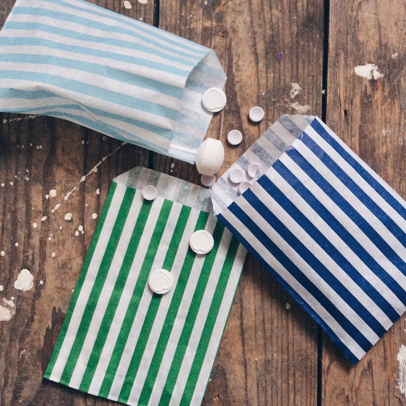 Pu&ograve; includere: Tre sacchetti di carta a righe con caramelle rotonde bianche sparse intorno. I sacchetti sono blu e bianco, verde e bianco e blu e bianco.