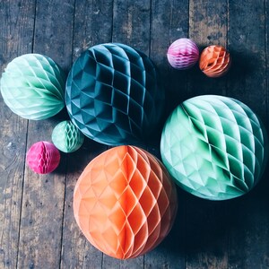 May include: A collection of colorful paper honeycomb balls in various sizes and shades of teal, green, pink, and orange. The decorative spheres are arranged on a rustic wooden surface, creating a visually appealing display.