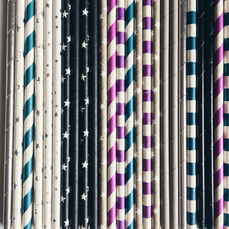 May include: A close-up of a variety of patterned paper straws. The straws are arranged in a row and feature different colors and patterns, including black and white stars, purple and white stripes, and teal and white stripes.