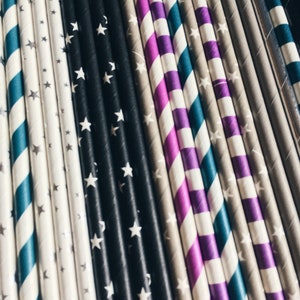 May include: A close-up of a variety of colorful striped paper straws with white stars. The straws are arranged in a row, with the black and white straws in the center.
