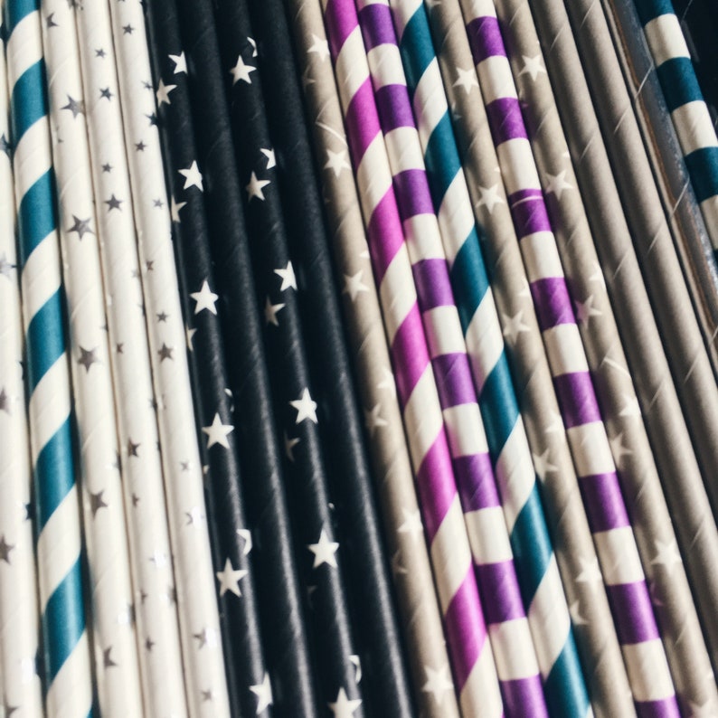 May include: A close-up of a variety of colorful striped paper straws with white stars. The straws are arranged in a row, with the black and white straws in the center.