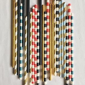 May include: A collection of colorful striped paper straws in red, white, blue, black, and gold. The straws are arranged in a vertical line.