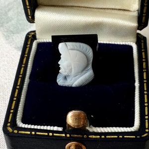 Peut inclure: Un camée blanc représentant une tête de profil, portant un casque, dans un écrin en velours noir avec un fermoir doré.