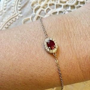 Peut inclure: Un bracelet en chaîne argent avec une pierre ovale rouge entourée de petites pierres blanches.