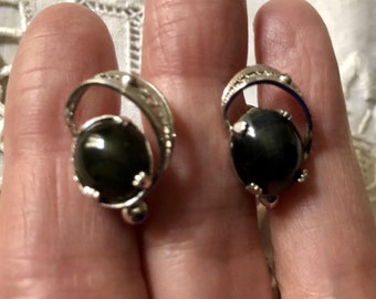 Könnte beinhalten: Ein Paar silberne Ohrringe mit schwarzen Edelstein-Akzenten. Die Ohrringe haben ein zartes, geschwungenes Design mit einem kleinen, runden Edelstein in der Mitte.